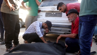 Friends and relatives mourn over the shrouded body of a man killed in an Israeli strike earlier, as he is brought to Deir al-Balah's Shuhada al-Aqsa hospital in the central Gaza Strip on October 19, 2025. (Photo by BASHAR TALEB / AFP)
