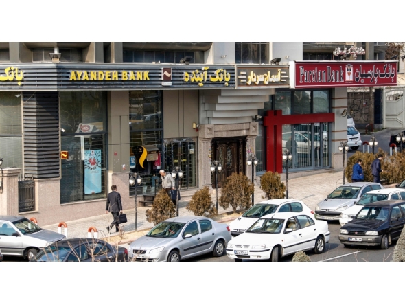 (Files) Iranians walk past an Ayandeh Bank branch (L) in the capital Tehran on January 14, 2017. (Photo by Atta Kenare / AFP)