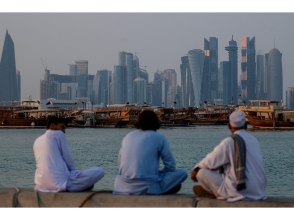 People sit along the corniche facing traditional dhow boats anchored in front of the Doha skyline on October 29, 2025. (Photo by Karim Jaafar / AFP)