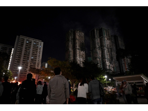 Bystanders look on after a major fire swept through several apartment blocks at the Wang Fuk Court residential estate in Hong Kong's Tai Po district on November 27, 2025. Residents anxiously awaited news of their loved ones on November 27 at a temporary shelter as one of Hong Kong's deadliest fires in decades engulfed a 2,000-unit high-rise complex. (Photo by Philip FONG / AFP)