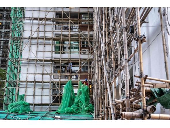 A construction worker removes the netting of bamboo scaffolding at Sui Wo Court housing estate in Fo Tan district of Hong Kong on December 4, 2025. (Photo by Philip Fong / AFP)