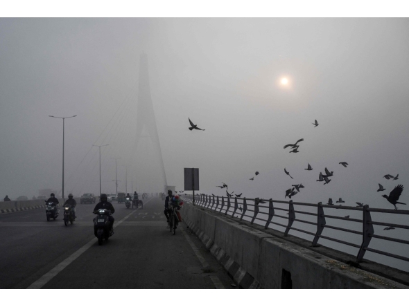 Commuters ride along the Signature Bridge over Yamuna river amid dense smog in NEW DELHI on December 27, 2025. (Photo by Arun SANKAR / AFP)