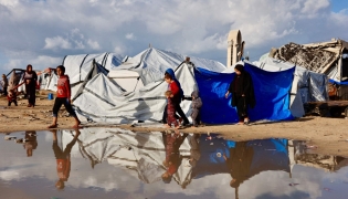 Displaced Palestinians walk past a large pool of rain water accumulated near tent shelters as the region experiences rain and cold winter conditions, in Gaza City on December 28, 2025. Photo by Omar AL-QATTAA / AFP