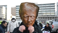 A protester wears a mask of US President Donald Trump during a rally condemning Trump's plans to raise tariffs in front of the US embassy in Seoul on January 27, 2026. (Photo by Jung Yeon-je / AFP)