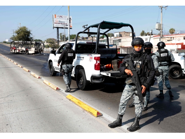 National Guard members stand guard near a burnt bus set on fire by organised crime groups in response to an operation in Jalisco to arrest a high-priority security target, at one of the main avenues in Zapopan, state of Jalisco, Mexico, on February 22, 2026. (Photo by Ulises RUIZ / AFP)