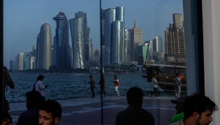 People sit with the reflection of the Doha skyline along the Doha Corniche in Doha on March 21, 2026. Photo by AFP