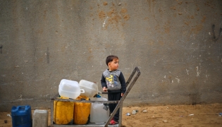 A displaced Palestinian boy stands on a trolley loaded with empty water canisters at the Nuseirat refugee camp, in the central Gaza Strip on April 1, 2026. (Photo by Eyad Baba / AFP)