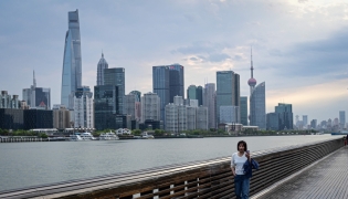 A woman walks along the Huangpu River as the city's skyline is seen in the background in Shanghai on April 9, 2026. (Photo by Jade Gao / AFP)