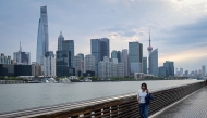 A woman walks along the Huangpu River as the city's skyline is seen in the background in Shanghai on April 9, 2026. (Photo by Jade Gao / AFP)