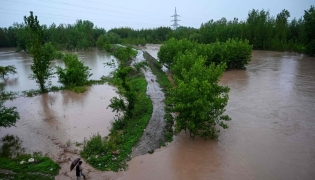 A man walks along a flooded path as torrential rains cause water channels to overflow, inundating nearby areas of Peshawar on April 7, 2026. Photo by Abdul MAJEED / AFP