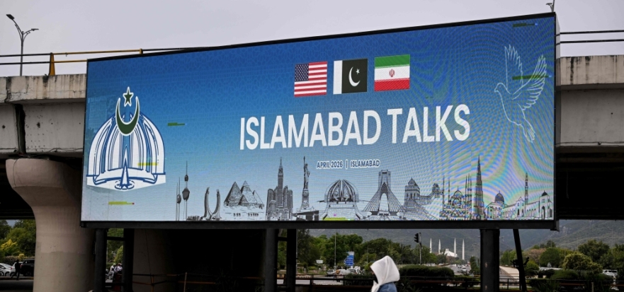 A woman walks past a digital screen displaying news of US-Iran peace talks along a road in Islamabad on April 10, 2026. (Photo by Farooq Naeem / AFP)