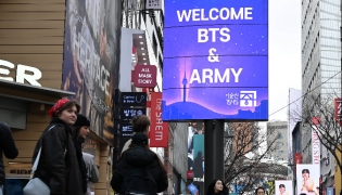 Tourists walk past a “Welcome BTS” sign in Myeong-dong, central Seoul, on Friday, a day ahead of the group’s comeback concert. (Lee Sang-sub/The Korea Herald)