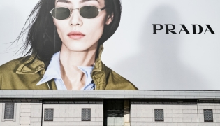 A man sits on a bench reading a newspaper next to a billboard of Italian luxury fashion brand Prada, on Navona Square on April 27, 2025. (Photo by Stefano RELLANDINI / AFP)
