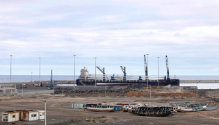A large cargo ship is seen behind migrant boats stacked at the port of Granadilla de Abona, on the island of Tenerife in Spain's Canary Islands archipielago, on May 6, 2026. (Photo by Oscar DEL POZO / AFP)