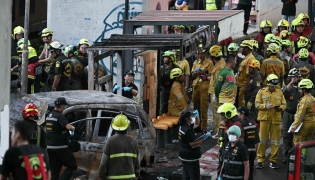 Forensic police officers, rescue workers and firefighters stand at the site of a train collision with a bus underneath Makkasan Airport Rail station in Bangkok on May 16, 2026. (Photo by Lillian SUWANRUMPHA / AFP)