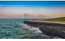 A runner is seen exercising along the Doha Corniche as waves splash along the shoreline e, with Doha's skyline standing prominently in the background. Pic: Qatarweather