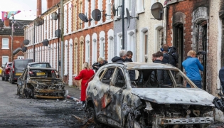 Residents and members of the media look at burnt-out cars and homes after demonstrations turned violent the night before, in eastern Belfast, Northern Ireland, on June 10, 2026. Photo by Paul Faith / AFP