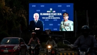Commuters ride past an electronic board featuring Pakistan's Prime Minister Shehbaz Sharif (L) with Army Chief and Field Marshal Syed Asim Munir, displayed along a road in Islamabad on June 18, 2026 after the US–Iran peace deal announcement. Photo by Aamir Qureshi / AFP