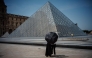 A couple protect themselves from the sun under an umbrella in front of the Louvre Pyramid, designed by Chinese-US architect Ieoh Ming Pei in Paris on June 23, 2026, as France experiences a heatwave. (Photo by Dimitar DILKOFF / AFP) 