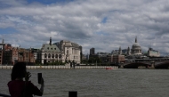 A woman takes a photo toward St. Paul's from the south side of the River Thames in central London on June 28, 2026, as people come out to take advantage of cooler temperatures following days of extreme heat. The UK broke the record for a June temperature for the third day in a row on June 26, the Met Office weather agency said, as a sweltering heatwave strained schools and hospitals and drove down business. (Photo by CARLOS JASSO / AFP)
