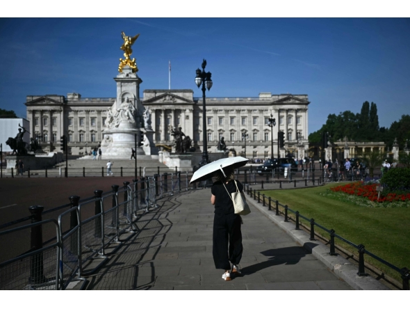 A person uses a parasol umbrella to shelter from the heat of the sun during a heatwave, as they walk near Buckingham Palace, in central London on July 7, 2026. (Photo by Justin Tallis / AFP)