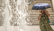 A woman protects herself from the sun with an umbrella as she walks through Athens' main square of Syntagman on July 21, 2026. (Photo by Aris Messinis / AFP)
 