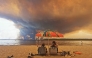 Beach goers sit on the beach of Moutchic in Lacanau, southwestern France on July 24, 2026, as clouds of smoke rise into the sky from a wildfire. Photo by Maximilien Lamy / AFP