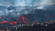This handout photograph taken by Etna Walk on August 11, 2026 and obtained on August 12, 2026 shows visitors standing next to lava flowing from Mount Etna volcano during an eruption, in Catania, in the Mediterranean island of Sicily. (Photo by Handout / Etna Walk / AFP)