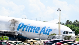 A parking lot filled with Tesla Cybercabs is seen in the foreground as the nose of a Prime Air cargo plane rests on the ground after the aircraft overran the runway and struck cars the previous day at Miami International Airport in Miami, Florida, on September 7, 2026. (Photo by CHANDAN KHANNA / AFP)