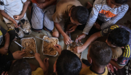 This photo taken on October 6, 2026, shows the children of Nihaya Al-Masri, sharing a meal provided by a charity kitchen in Khan Yunis, in the southern Gaza Strip. (Photo by Bashar Taleb / AFP)