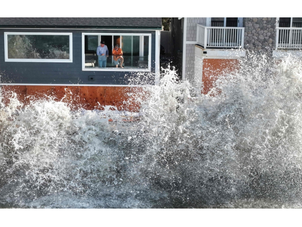 In an aerial view, people watch from a home as a Pacific Ocean wave crashes into a seawall protecting homes amid powerful surf on October 9, 2026 in Long Beach, California. (Photo by Mario Tama/Getty Images/AFP ) 