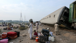  Passengers sit with their belongings next to derailed coaches of the passenger train Rehman Baba Express on the outskirts of Multan on October 13, 2026. (Photo by Shahid Saeed MIRZA / AFP)