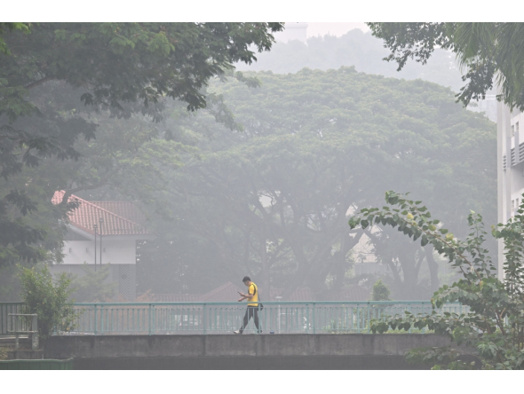 This picture provided by The Straits Times taken and received on October 14, 2026 shows a man walking on a road as the city is shrouded with haze in Singapore. (Photo by The Straits Times / AFP)