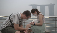 Tourists wear protective masks while seated across Marina Bay Sands in Singapore on October 15, 2026, as the country continues to be shrouded in haze caused by fires in Indonesia / AFP