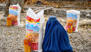 An Afghan burqa-clad woman sits next to food aid distributed by a local charity foundation in Mazar-i-Sharif. (AFP)