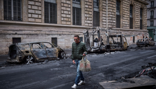 A man walks past a row of burnt out vehicles on Rue Yves Toudic destroyed after a nationwide protest against the 