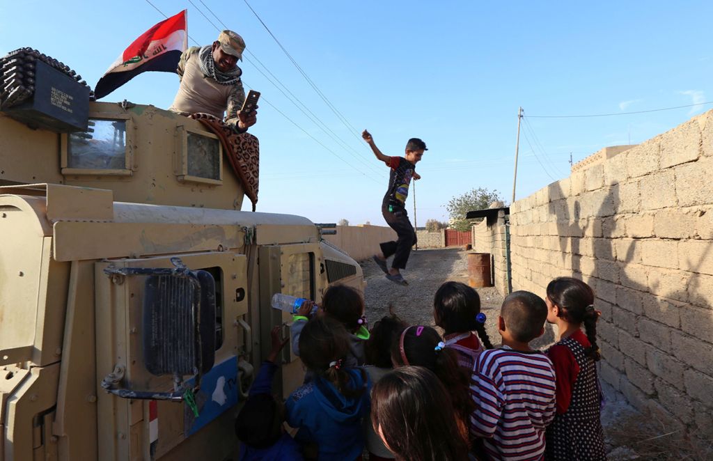 Children gather next to an Iraqi forces vehicle patrolling a street in the village of Jarif, some 45 kilometres south of Mosul, on November 12, 2016, after retaking it from Islamic State (IS) group jihadists. / AFP / SAFIN HAMED
