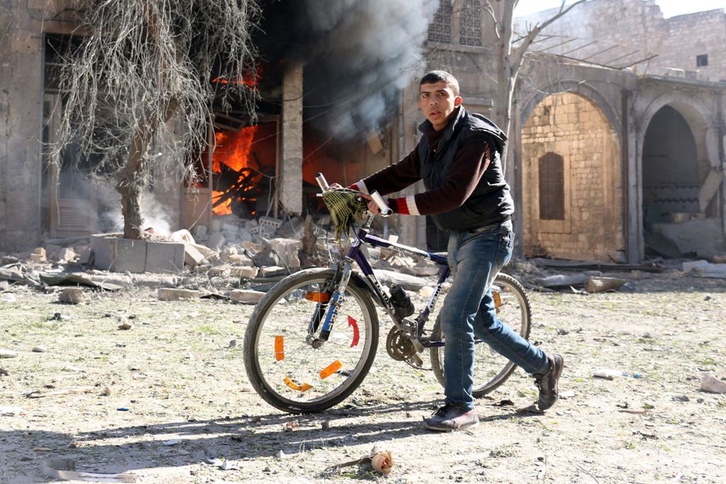 A Syrian youth pushes his bicycle past a burning house on November 19, 2016 following a reported air strike on Aleppo's rebel-held neighbourhood of Bab al-Nayrab. AFP / AMEER ALHALBI