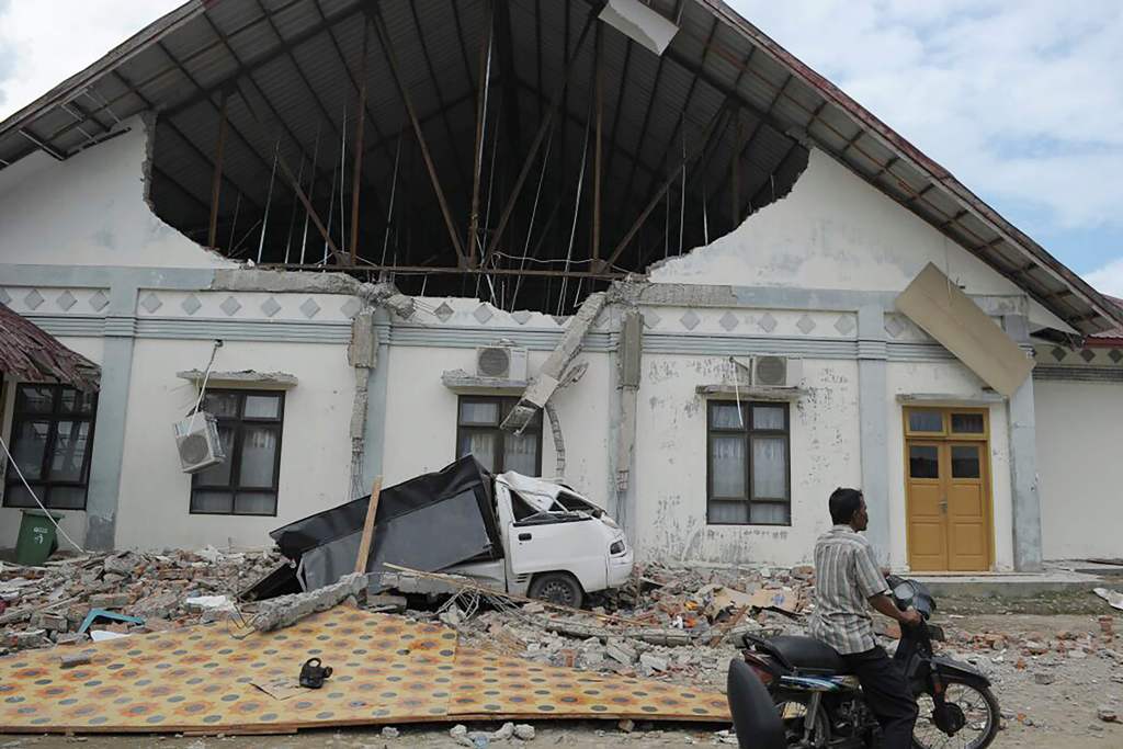 TOPSHOT - a man rides past a district hospital which was damaged after an earthquake in Pidie Jaya, Aceh province on December 7, 2016. At least 52 people were killed and hundreds injured on December 7 after a strong earthquake struck Indonesia's Aceh prov