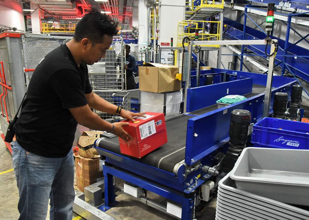 This photograph taken on December 5, 2016 shows a worker placing inbound parcels on a conveyor belt for coding at the sorting section of the Singapore Post (SingPost) ecommerce logistics centre in Singapore. AFP / Roslan RAHMAN 