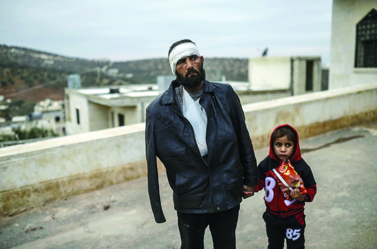 An injured man who just arrived on the Syrian side of the Bab Al Hawa border waits with his child outside a hospital, yesterday.