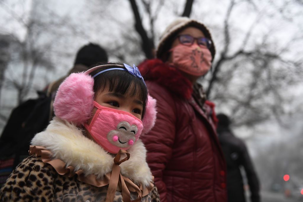 A young girl waits by the road with a relative on a heavily polluted day in Shijiazhuang, in northern China's Hebei province on December 21, 2016. China's smoggiest city closed schools December 21 as much of the country suffered its sixth day under an opp