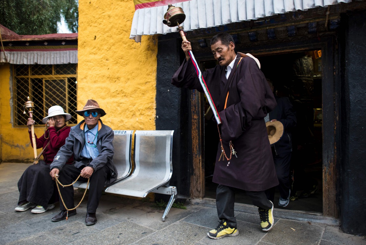 A pilgrim spinning his prayer wheel in front of the 'Thousand Buddha Cliffside Sculpture' on September 10, 2016 in the regional capital Lhasa, in China's Tibet Autonomous Region. AFP / Johannes EISELE