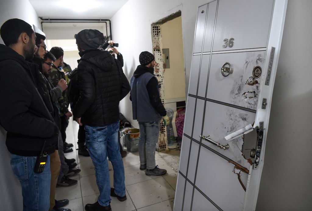 Turkish plain clothes police officers wait next to a damaged door at the apertment where the main suspect in the Reina nightclub rampage was arrested by Turkish police the night before, in Istanbul on January 17, 2017.  AFP / OZAN KOSE