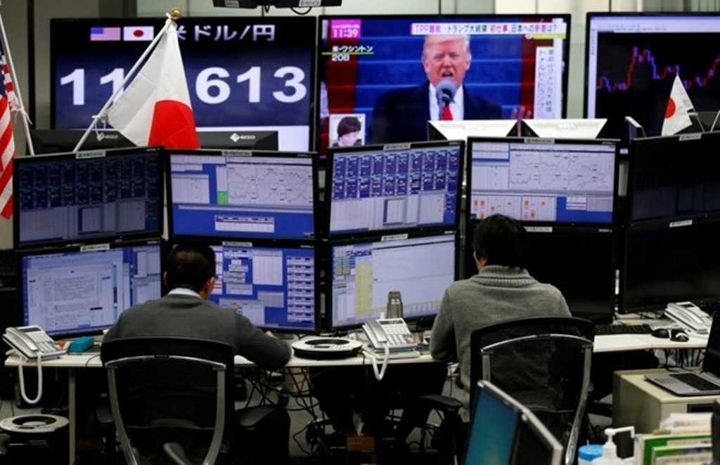 Employees of a foreign exchange trading company work near monitors showing U.S. President Donald Trump (top C) and the Japanese yen's exchange rate against the U.S. dollar in Tokyo, Japan, Jan. 23, 2017. REUTERS/Toru Hanai.