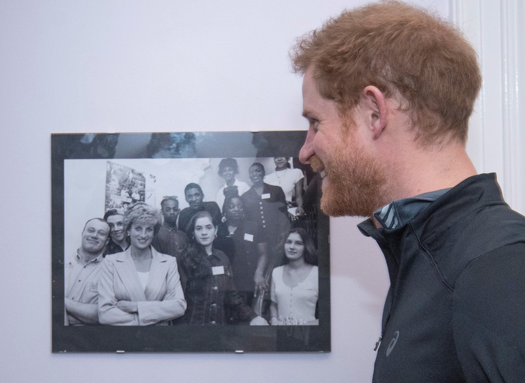 Britain's Prince Harry (R) looks at a photo of his mother, Princess Diana, posing with staff and service users of The Running Charity in northwest London on January 26, 2017 as Prince Harry visits the charity to learn about its activities.  AFP / POOL / G