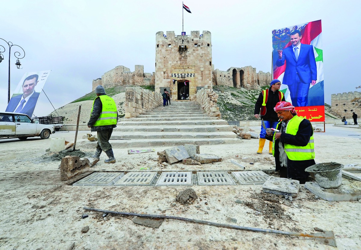Workers repair the damage in front of Aleppo's historic citadel, as posters depicting Syria's President Bashar Al Assad are erected in the Old City of Aleppo, yesterday.