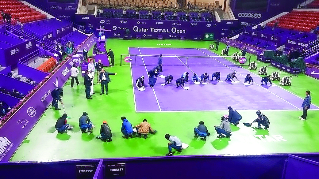Workers mop up the playing surface as play was stopped due to rain during the Qatar Total Open at the International Khalifa Tennis Complex in Doha yesterday. Picture by Anvar Sadath
