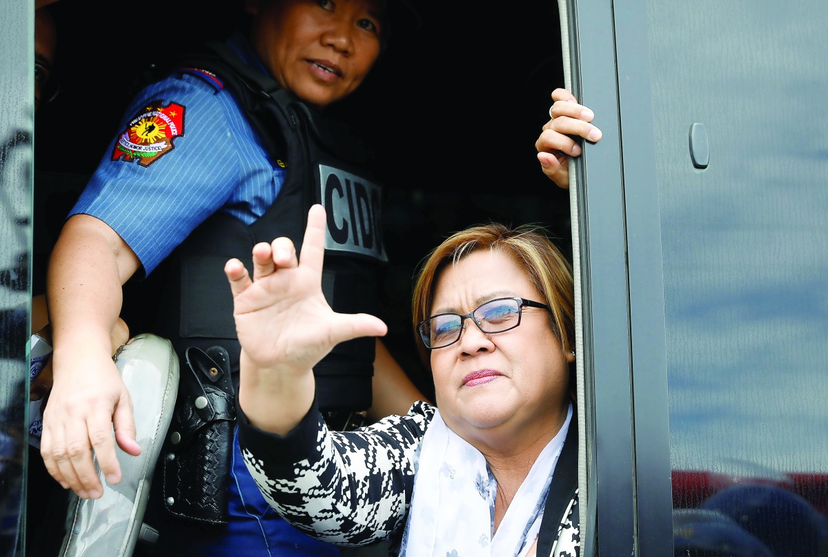 A policewoman guards Philippine Senator Leila De Lima as she gestures a sign that means 