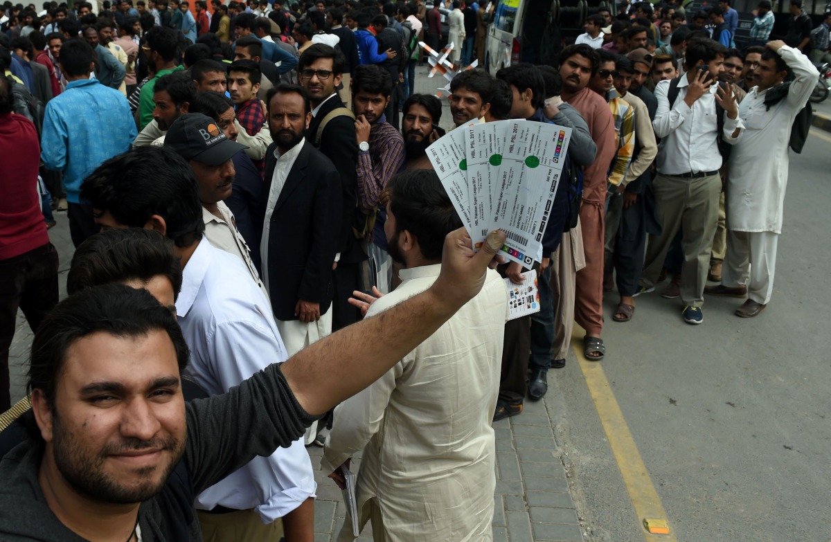 A Pakistani cricket fan poses showing his tickets of the forthcoming Pakistan Super League (PSL) final cricket match as others stand in a queue outside a bank in Lahore. (AFP / ARIF ALI)
